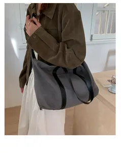 Close-up of a large grey canvas tote bag with black leather straps on a model's shoulder