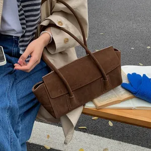 Brown suede underarm bag with double straps shown in a stylish outdoor street fashion setting