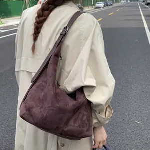 Sac hobo marron foncé en daim synthétique porté par un mannequin en extérieur