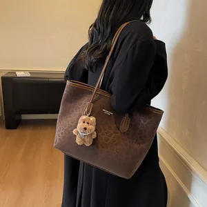 Large leopard print tote bag with plush puppy charm worn by model in a black coat