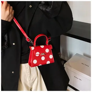 Detailed shot of red polka dot handbag featuring a metallic twist lock and slim strap