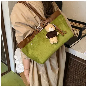 Detail of green suede tote bag with brown trim and cute plush bear accessory