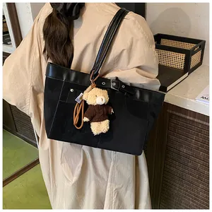 Detail of black canvas tote bag with decorative buckle and cute brown bear plush charm