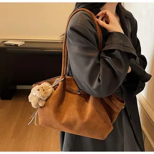 Détail d'un sac bandoulière en daim marron avec une breloque chiot en peluche blanche