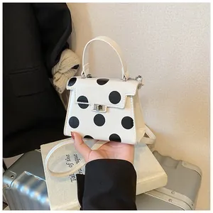 Detailed view of white polka dot handbag with silver twist lock and slim shoulder strap