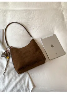 Detail of dark coffee suede shoulder bag with heart pendant next to a tablet