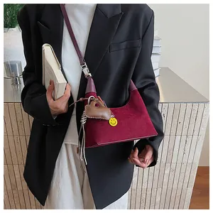 Detail of burgundy suede hobo bag with heart pendant worn with a black blazer