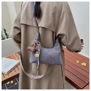 Grey suede crescent shoulder bag with cute charms worn with a stylish trench coat