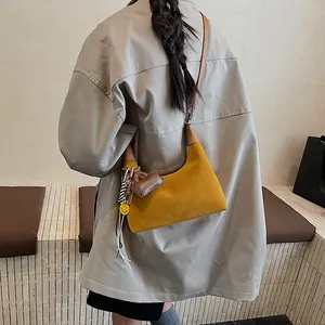 Chic mustard suede bucket bag with brown strap and decorative charms for shoulder wear