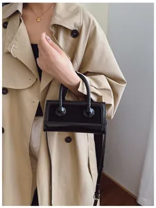 Glänzende schwarze Mini-Handtasche mit runden Schnallen am beigen Trenchcoat
