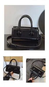 Detail einer schwarzen glänzenden Lackleder-Box-Tasche mit Doppelgriffen und Gurt