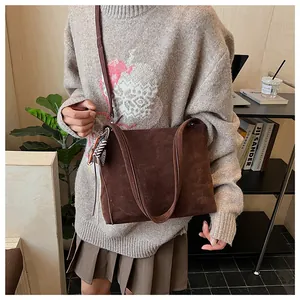 Dettaglio di una borsa tote in pelle scamosciata marrone scuro con ciondolo intrecciato