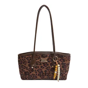 Fashionable leopard print tote bag with brown leather handles and beaded charm accessory