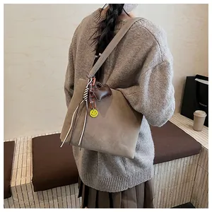 Dettaglio della borsa tote in pelle scamosciata marrone con ciondoli su maglione autunnale