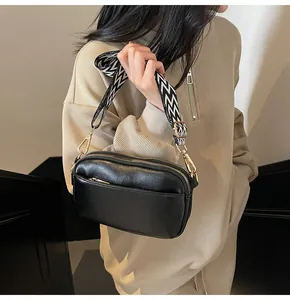 Detail van zwarte crossbody tas met geometrische band en goudkleurige rits sluitingen