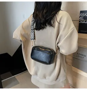 Crossbodytas met brede geometrische geweven riem op een beige gestreepte sweater