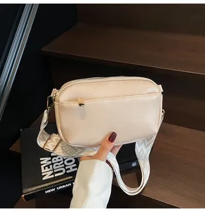 Detail van beige PU-leren schoudertas met geweven riem en goudkleurige ritssluiting