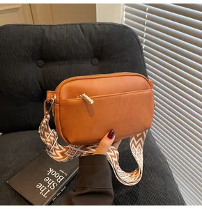 Detail van bruine lederen crossbodytas met geweven riem en goudkleurige metalen beslag