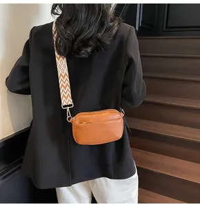 Detail van bruine lederen crossbodytas met brede geweven schouderband met patroon