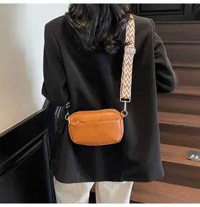 Detail van een karamel lederen crossbodytas met een brede geweven riem op een model