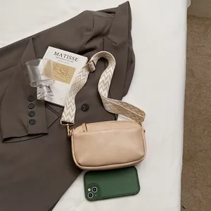 Minimalistische beige crossbodytas met geometrische riem naast een smartphone