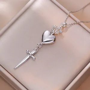 Detailed shot of silver heart and dagger pendant necklace on champagne silk