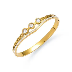 Detail van een golfvormige goudkleurige armband met drie ronde stenen en zijdelingse diamanten