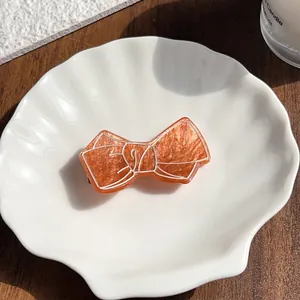 Détail d'une pince à cheveux nœud orange avec texture marbrée sur un plat blanc