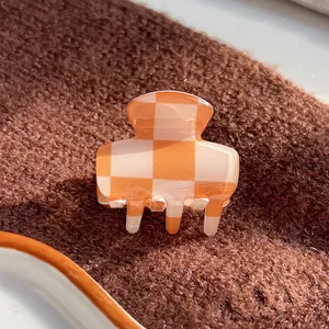 Close-up of small orange and white checkered hair claw clip on soft brown knit fabric