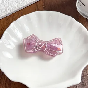 Gros plan sur une pince à cheveux nœud rose translucide avec des paillettes d'or