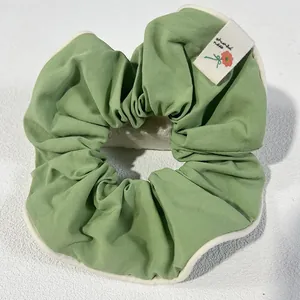 Green fabric scrunchie with cream piping and a floral tag for stylish updos