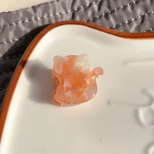 Macro detail of cat-shaped acetate hair claw featuring orange marble texture on ceramic plate