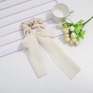 French style beige hair scrunchie with long lace streamers shown on a wooden background