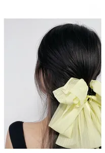 Détail d'une grande pince à cheveux à nœud jaune pâle sur cheveux longs et sombres