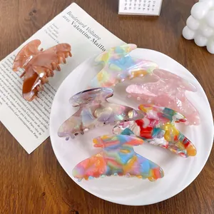 Set of six colorful acetate hair claw clips with marble and amber patterns in a dish