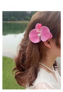 Detail view of a pink orchid hair clip with a central pearl worn on a woman's side profile