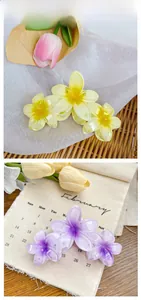 Détail de deux pinces à cheveux fleur de frangipanier en résine jaune et violette brillante