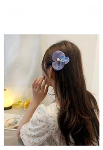 Detail of a purple tulle orchid hair clip with pearl center on model's hair