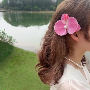 Pink phalaenopsis orchid hair clip with pearl detail worn by model in nature