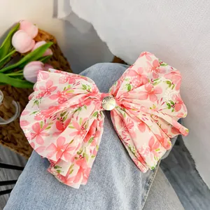Dettaglio di un grande fiocco per capelli a fiori rosa in chiffon plissettato su denim