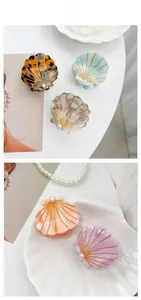 Shell-shaped hair claws with golden stripes and white pearl detail on white background