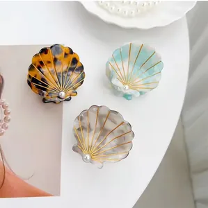 Three acetate shell hair claws with gold details and pearls on a white background