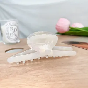 Dettaglio di un fermaglio per capelli in acetato bianco perla a forma di conchiglia