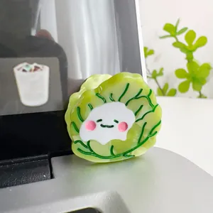 Close-up of cute cartoon cabbage hair clip with smiling face on laptop surface