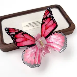 Pink gradient acrylic butterfly hair claw clip with realistic wing patterns on a wood tray