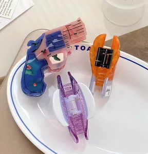 Three creative acetate hair claws in playful gun and wing shapes on a ceramic tray