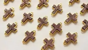 Makro-Detail von vergoldeten Kreuz-Verbindern mit funkelndem lila Inlay für DIY-Schmuck