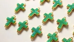 Makroaufnahme von 12 grünen Kreuzanhängern mit Goldbeschichtung für die Schmuckherstellung