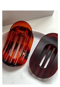 Close-up of matte brown and amber oval hair clips on a white textured tray