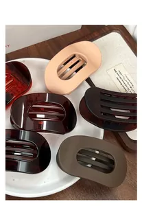 Close-up of matte flat oval duckbill hair clips in assorted colors on a white tray